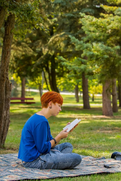 Rudowłosa dziewczyna czyta książkę na polanie w parku.