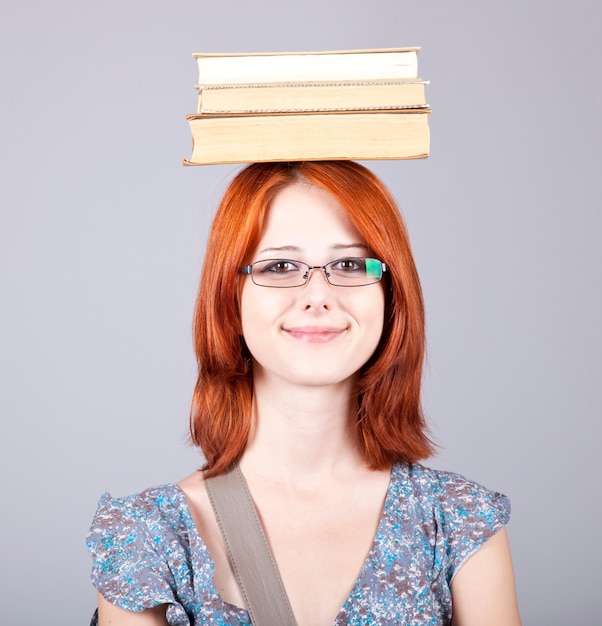 Rudowłosa dziewczyna trzyma książki na głowie. Strzał studio.