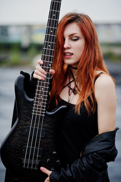 Rudowłosa kobieta punk nosi na czarno z gitarą basową na dachu.