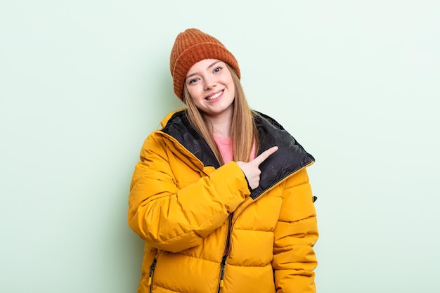 Zdjęcie rudowłosa kobieta uśmiechając się radośnie, czując się szczęśliwa i wskazując na bok. koncepcja zima