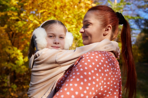 Rudowłosa szczęśliwa kobieta z córeczką w ramionach w jesiennym, słonecznym parku