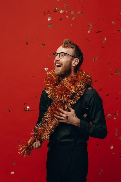 Rudowłosy wesoły mężczyzna w okularach i złotym boa na imprezie noworocznej z konfetti Fotografia studyjna