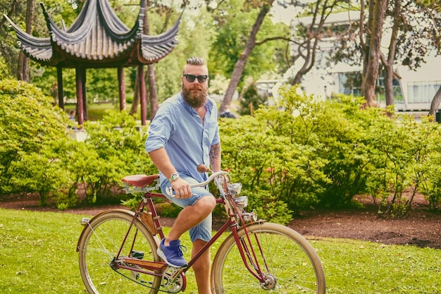 Rudy brodaty mężczyzna hipster na rowerze retro w letnim parku.