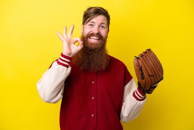 Rudy gracz z brodą z rękawicą baseballową na białym tle na żółtym tle pokazującym znak ok palcami