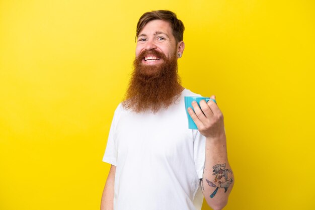 Rudy mężczyzna z brodą, trzymający kubek na białym tle na żółtym tle, często się uśmiecha