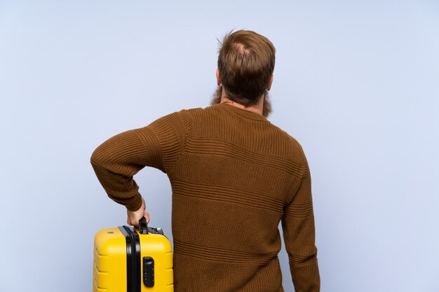 Rudy mężczyzna z długą brodą trzyma walizkę w tylnej pozycji