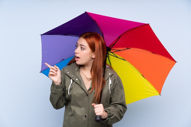 Rudzielec nastolatka dziewczyna trzyma parasol nad niebieskim palcem wskazującym na bok