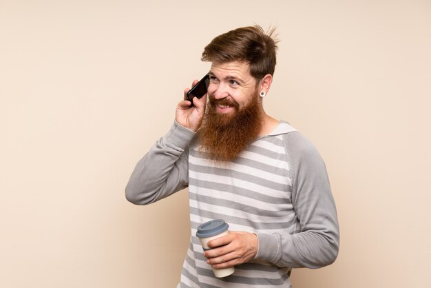 Rudzielec z długą brodą trzyma kawę na wynos i telefon komórkowy