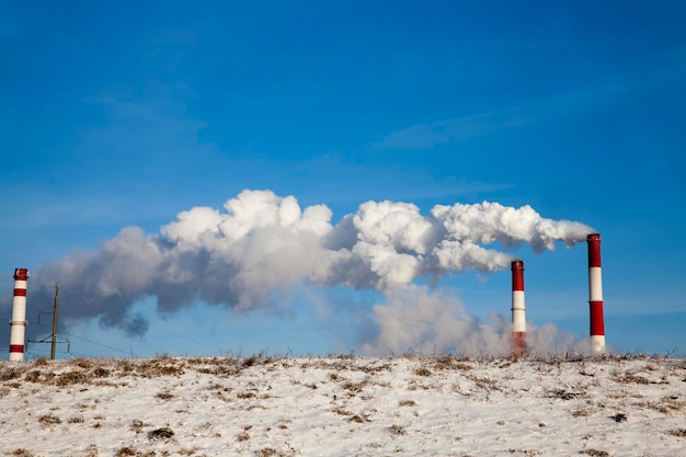rury elektrociepłowni przedsiębiorstwa spalające paliwo i emitujące dużą ilość dymu i emisji do atmosfery, rury przemysłowe z białym dymem zimą