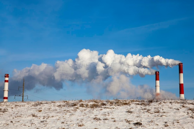 Rury elektrociepłowni przedsiębiorstwa spalającego paliwo i emitującego dużą ilość dymu i emisji do atmosfery Rury przemysłowe z białym dymem w zimie