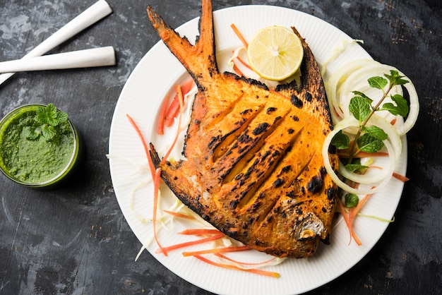 Ryba Tandoori Pomfret gotowana w glinianym piecu i przyozdobiona sałatką z cytryny, mięty, kapusty i marchewki. Selektywne skupienie