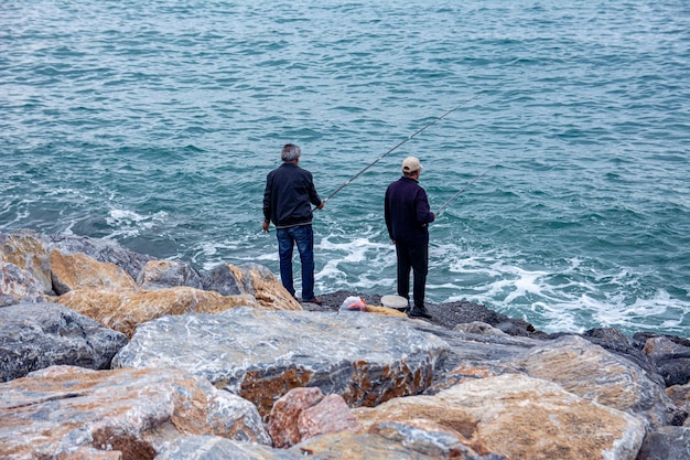 Rybacy łowią ryby siedząc na kamieniach na nadmorskiej promenadzie w pochmurny dzień