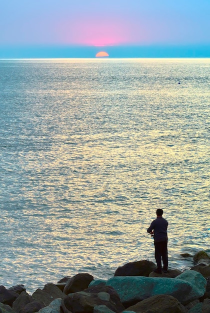 Rybak na wybrzeżu Morza Czarnego Mężczyzna z wędką wśród kamieni zachodzące słońce