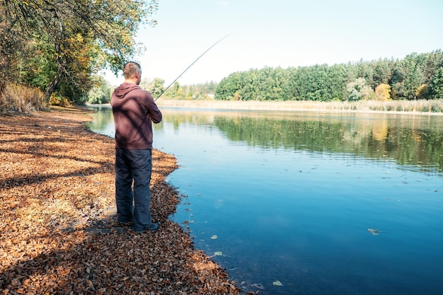 Rybak z wędką spinningową na jesiennym jeziorze rybak z spinningiem w dłoniach łowi ryby w