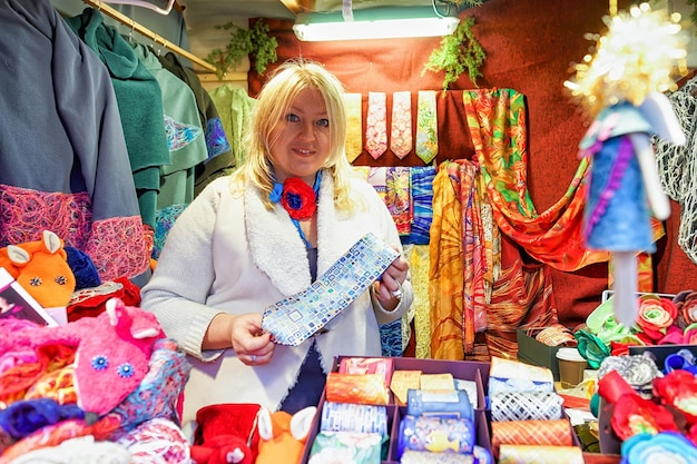 Ryga, Łotwa - 25 grudnia 2015: Śliczna łotewska kobieta oferuje świąteczne krawaty na swoim straganie podczas jarmarku bożonarodzeniowego w Rydze. Na targu można kupić tradycyjne jedzenie, ciepłe ubrania i pamiątki.