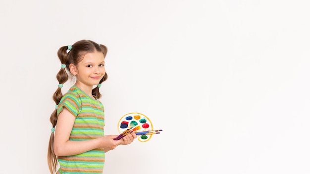 Rysunek dla dzieci w wieku szkolnym Mała dziewczynka w topie z paletą farb i pędzli pokazuje Twoją reklamę na białym tle