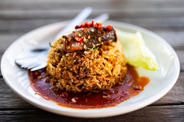 Ryż smażony z konserwowaną makrelą na białym talerzu na drewnianym stole w stylu tajskim