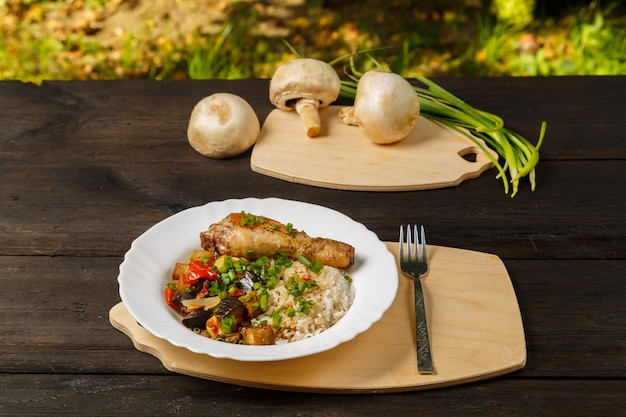 Ryż z duszonymi warzywami i pieczonym udkiem z kurczaka na ręcznie robionej drewnianej desce obok pieczarek i zielonej cebuli