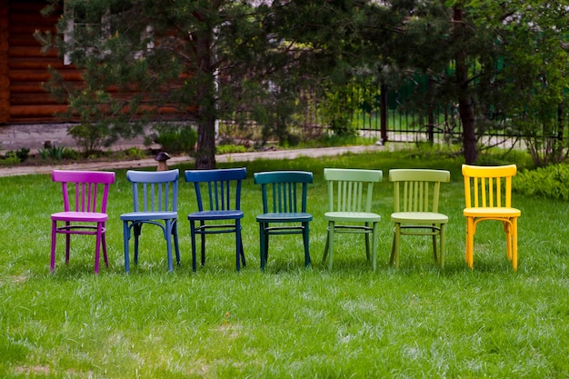 Rząd kolorowych tęczowych drewnianych krzeseł na zielonym trawniku impreza społeczności lgbt w parku w m...