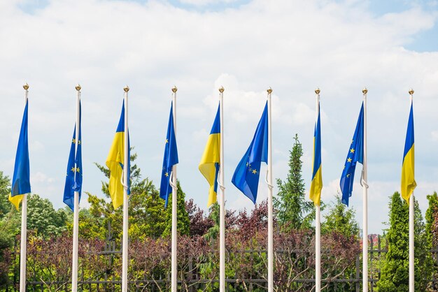 Rząd masztów flagowych z flagami Unii Europejskiej i Ukrainy powiewającymi na wietrze na tle błękitnego nieba