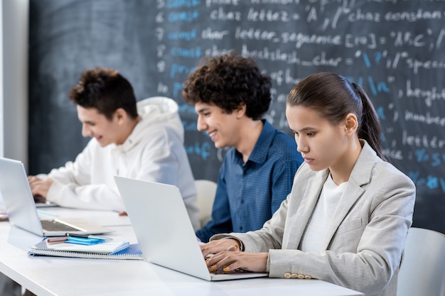 Rząd młodych współczesnych studentów pracujących przy biurku przed laptopami