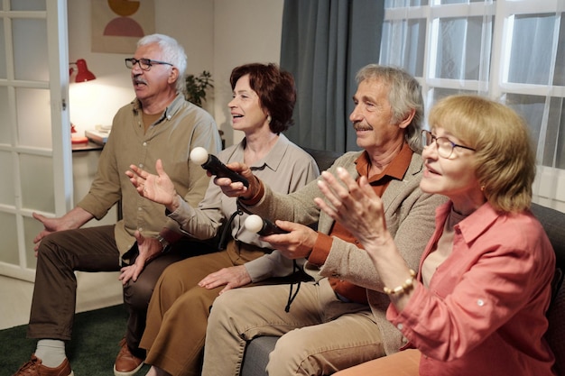 Rząd przyjaznych seniorom mężczyzn i kobiet siedzących na kanapie i grających w gry wideo