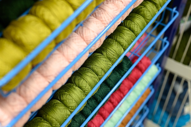 Rzędy kuleczek kolorowych nici z przędzy bawełnianej do robienia na drutach jasnoróżowych i zielonych kolorów na półkach w sklepie