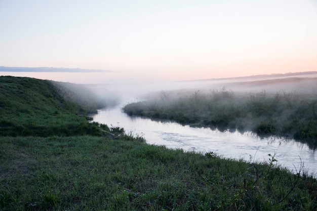 Rzeka płynąca przez zielone łąki z wysoką trawą mglistą wczesnym rankiem Region Uljanowsk Rosja