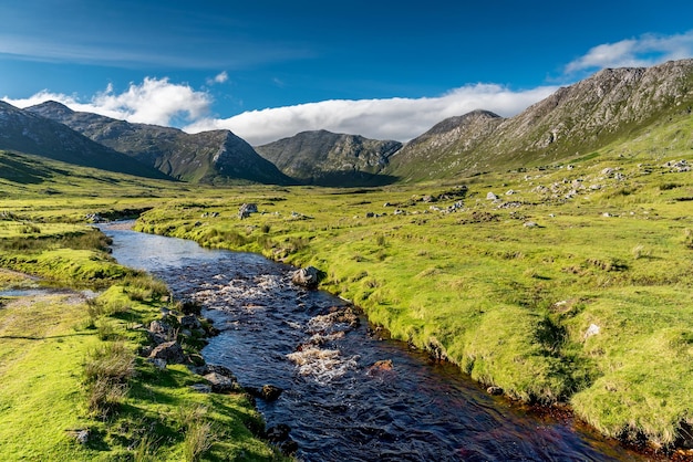 rzeka płynie wśród łąk przed majestatycznymi górami Twelve Bens w Connemara w Irlandii