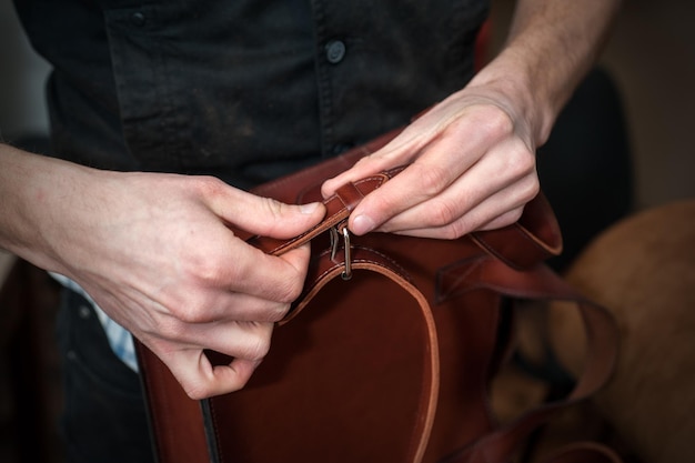 Rzemieślnik w warsztacie mocuje pasek na ramię do gotowej ręcznie robionej skórzanej teczki