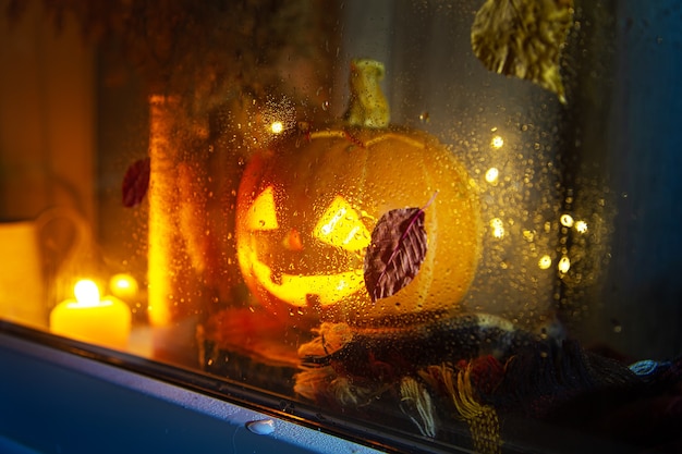 Rzeźbiona dynia wygląda przez okno. Jack Lantern, koncepcja Halloween. Deszczowo, jesień. Skoncentruj się na szkle.