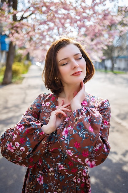 Sakura rozgałęzia się kwiatami na drzewie na ulicach miasta. Szczęśliwa kobieta dziewczyna przędzenia na ulicy z kwitnącą sakura. Sakura kwitnie.