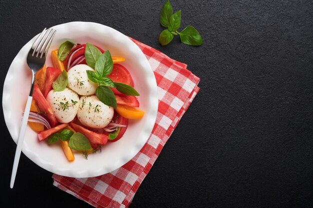 Sałatka caprese Włoska sałatka caprese z plastrami pomidorów ser mozzarella oliwa z bazylii oliwa z oliwek na białym talerzu na czarnym tle Pyszne włoskie jedzenie Widok z góry Styl rustykalny