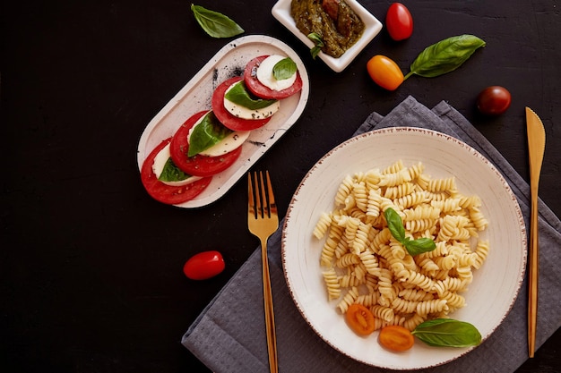 Sałatka Caprese z mozzarellą pomidorową i bazylią z pesto Włoski makaron fusilli na czarnym tle rustykalnym Widok z góry