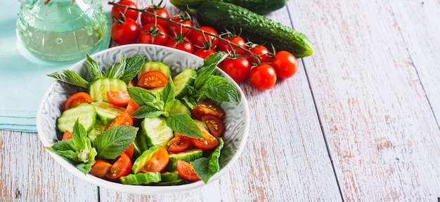 Sałatka dietetyczna z ogórków, pomidorów i mięty w misce i warzyw na banerze internetowym stołu