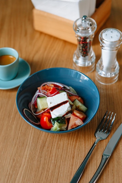Sałatka grecka z serem feta i świeżymi warzywami stojąca na stole w jadłodajni widelec obok szklanka kawy śniadanie