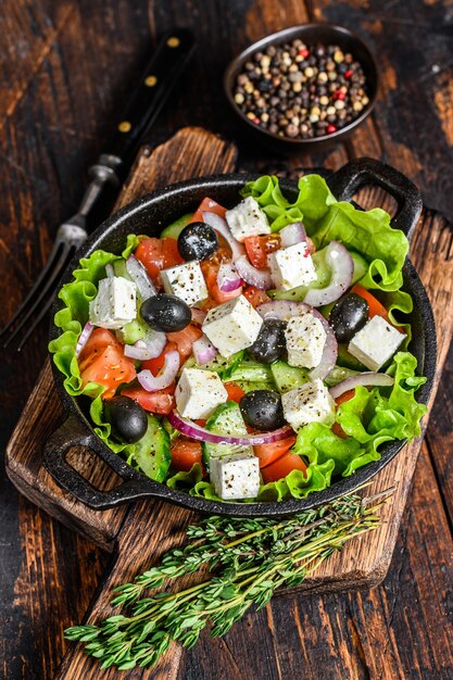 Sałatka grecka ze świeżymi warzywami i serem feta na patelni. Ciemne drewniane tło. Widok z góry.