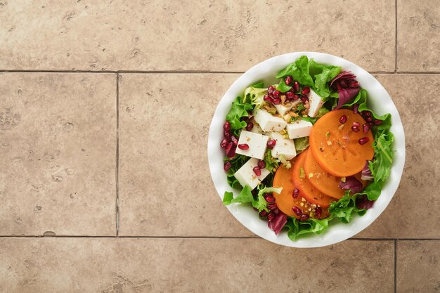 Sałatka Świeża zielona sałatka z serem feta persimmon granatem i pistacjami na białym talerzu Pomysł na zdrową pyszną zimową sałatkę świąteczną Zdrowe zrównoważone odżywianie Widok z góry