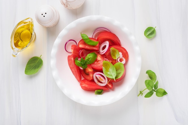 Sałatka ze świeżych pomidorów z liśćmi bazylii oliwą z oliwek i cebulą w białej misce na jasnym tle Tradycyjna włoska lub śródziemnomorska dieta jedzenie Widok z góry