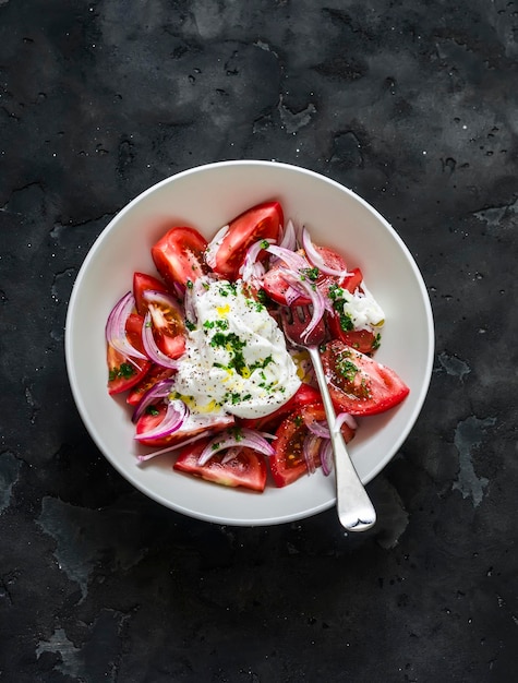 Sałatka ze świeżymi pachnącymi pomidorami burrata, czerwoną cebulą i sosem pesto na ciemnym tle widok z góry