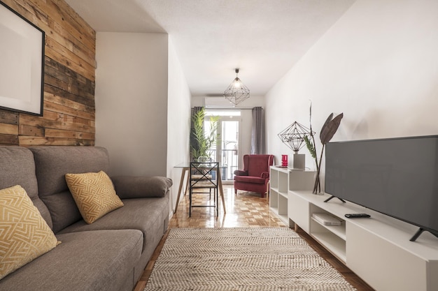 Salon decorado con paredes de madera sin barnizar en apartamento de alquiler a corto plazo con aparador blanco con tv y suelo de parquet de roble alfombra de fibra y sillon rojo