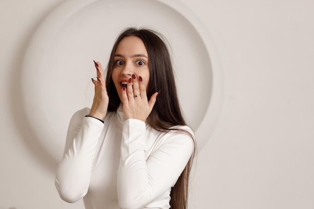 Salowy portret pozytywnej zdziwionej brunetki młodej kobiety na białym tle