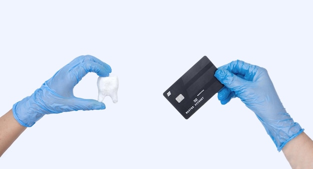 Samica dentysta ręka w niebieskich rękawiczkach posiada dentystę Model zęba i kartę kredytową Jasne tło Koncepcja kosztów leczenia stomatologicznego