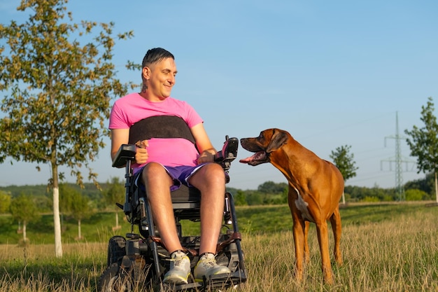 Samiec na czarnym wózku inwalidzkim bawi się ze swoim psem na rozświetlonym łące