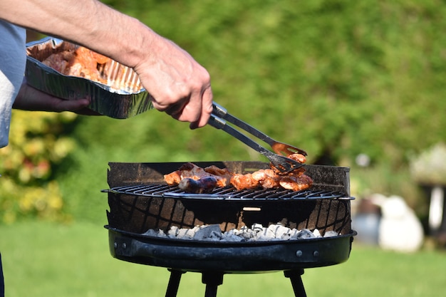Samiec używa pincety do przygotowania udka z kurczaka na grillu w ogrodzie z tyłu