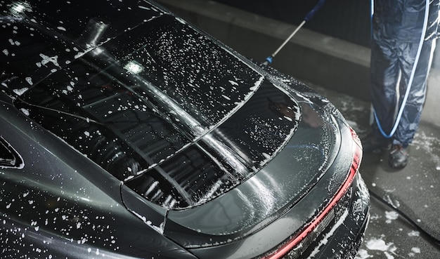 Samochód luksusowy pokryty wodą i proszkiem podczas prania pod ciśnieniem w myjni samochodowej