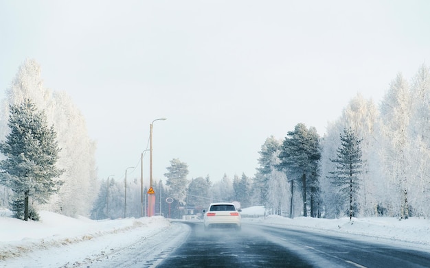 Samochód na zimowej drodze ze śniegiem w Finlandii. Auto i zimny krajobraz Laponii. Samochód w lesie Europy. Jazda autostradą po fińskim mieście. Drogą i trasą zaśnieżoną ulicę. Napędowy