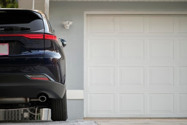 Samochód zaparkowany przed szerokimi podwójnymi drzwiami garażowymi na betonowym podjeździe nowego nowoczesnego amerykańskiego domu