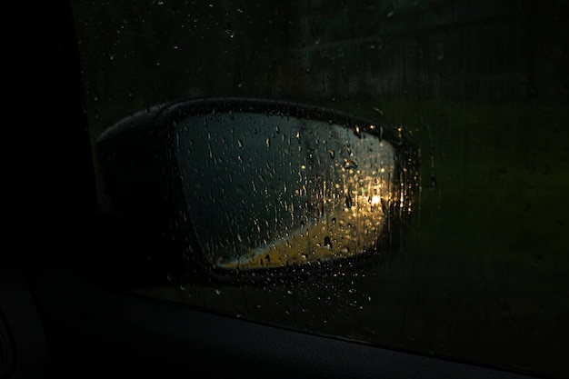 Samochodowe lusterko boczne z odbiciem reflektorów w deszczu
