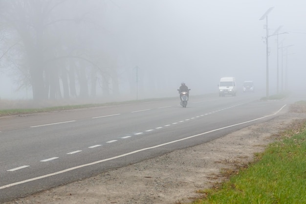 Samochody i skuter we mgle Zła zimowa pogoda i niebezpieczny ruch na drodze Lekkie pojazdy w mglisty dzień Sezonowe ostrzeżenie o niebezpieczeństwie wypadków przy złej deszczowej pogodzie